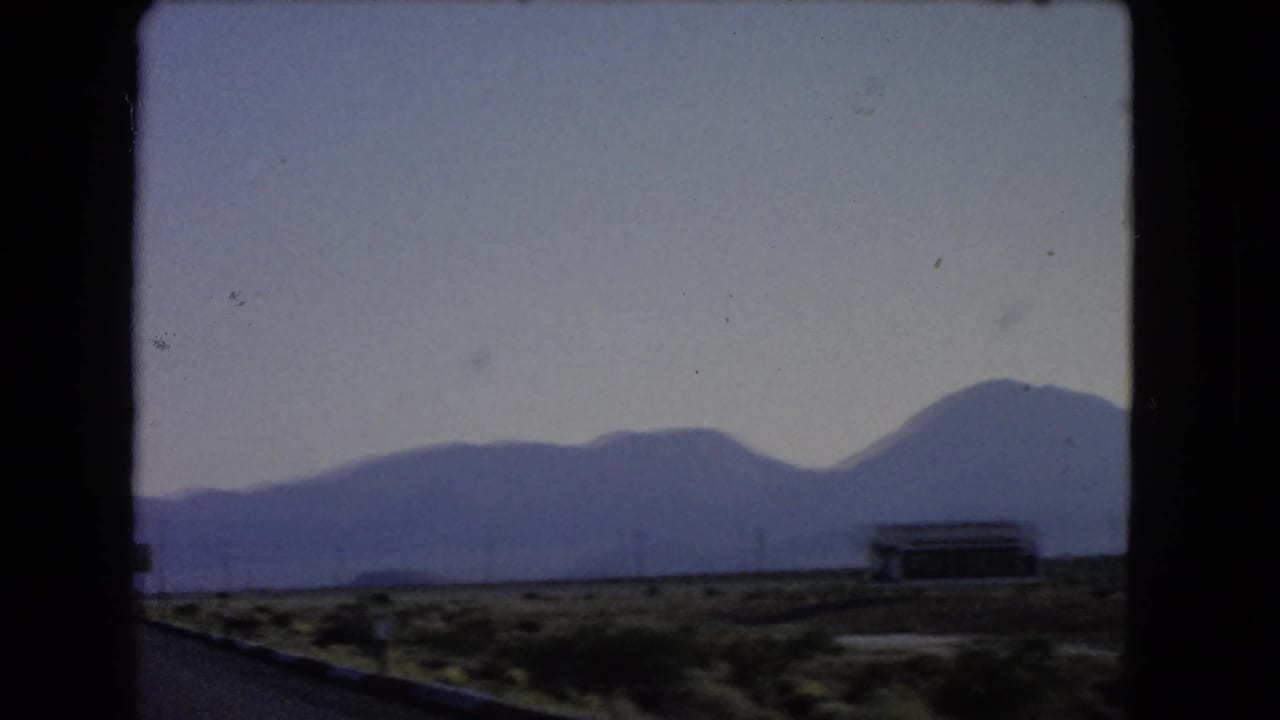 Desert roadside with distant mountains, a low structure, and dark 8mm frame edges.