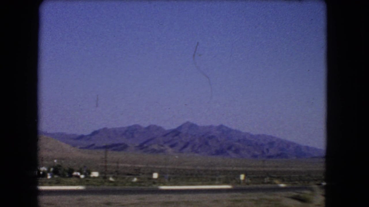 1966 Nevada road-travel view from a moving vehicle, showing desert terrain and distant mountains beyond the highway.