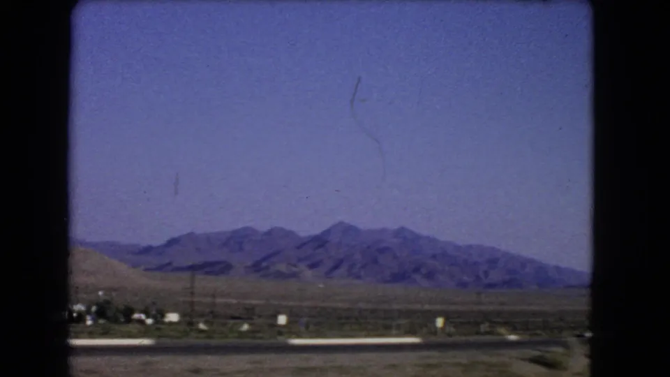 1966 Nevada road-travel view from a moving vehicle, showing desert terrain and distant mountains beyond the highway.