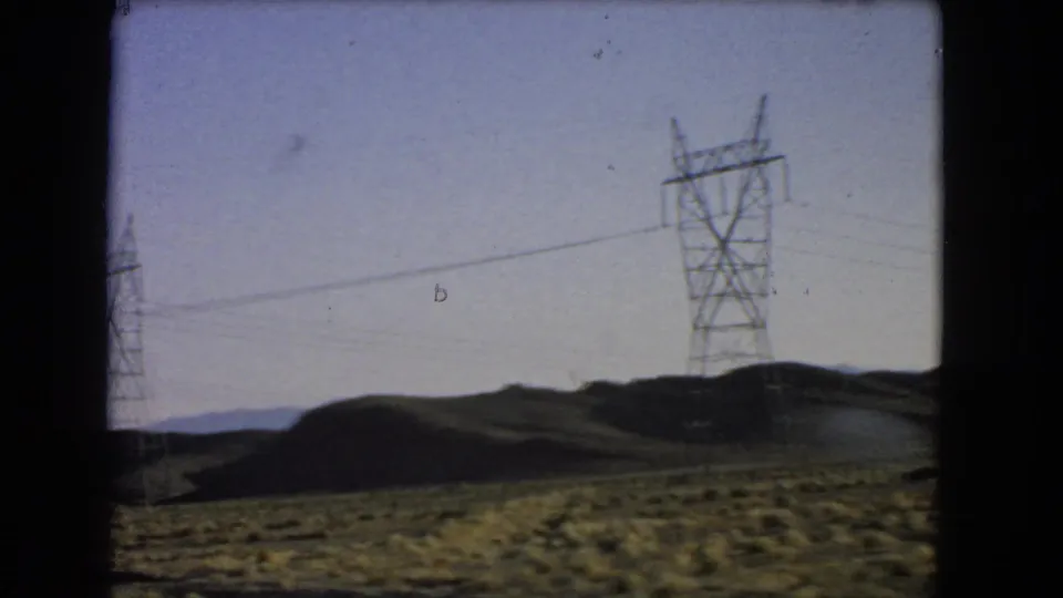 Power pylons and overhead lines stretch across low desert hills in vintage 8mm Nevada travel footage.