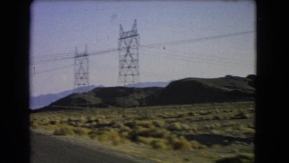 Moving-vehicle view of a Las Vegas-area desert road lined with utility towers and distant mountain ridges.