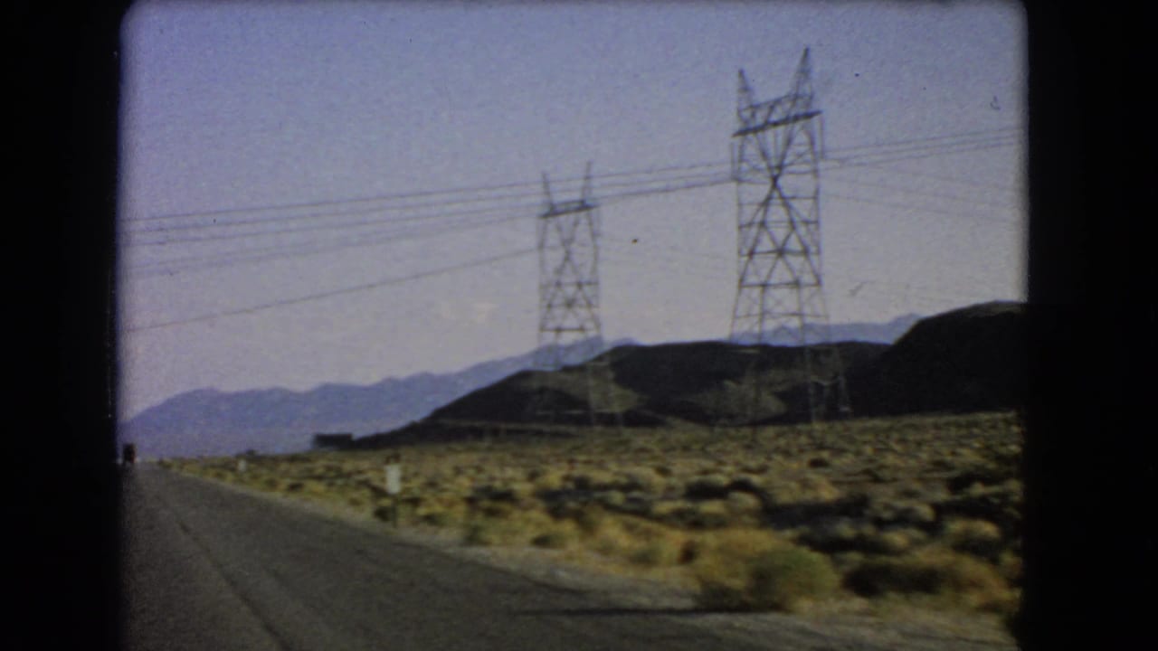 1966 Nevada desert road scene with utility towers and wires stretching across hills and distant mountains.