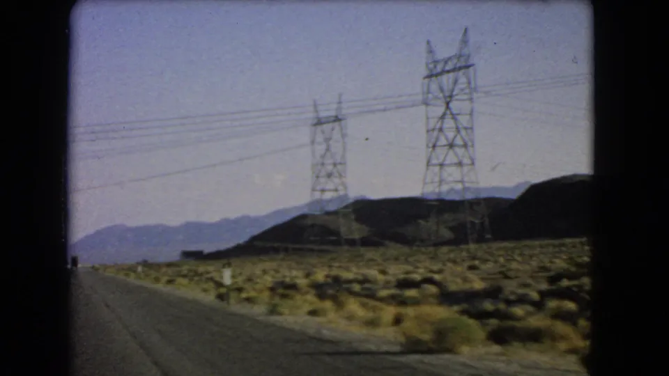 1966 Nevada desert road scene with utility towers and wires stretching across hills and distant mountains.