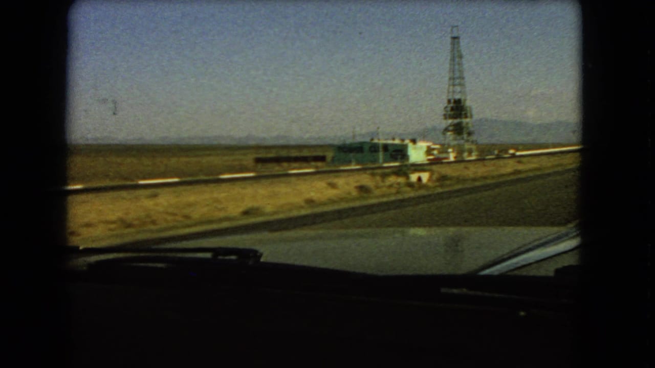 Las Vegas-area roadside view from inside a moving car, showing a low structure and tall derrick-like tower in the desert.
