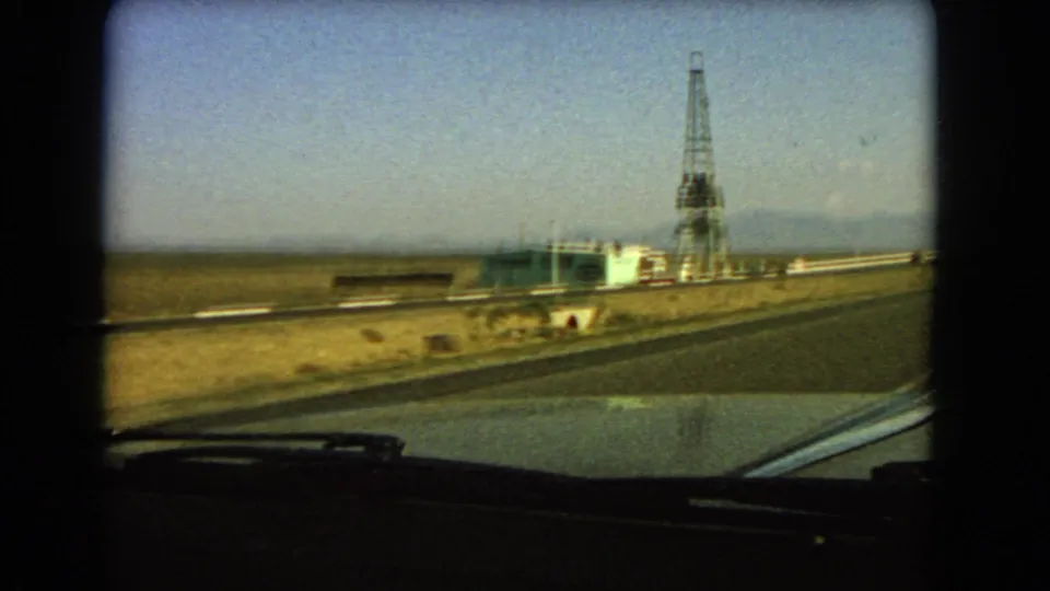 1966 Las Vegas-area 8mm view from a moving car toward a roadside tower, low building, dry valley, and distant mountains.