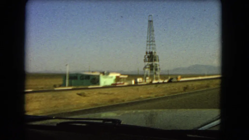 Late shot from the moving car shows the tower and low building receding along a Las Vegas-area desert road in 1966.