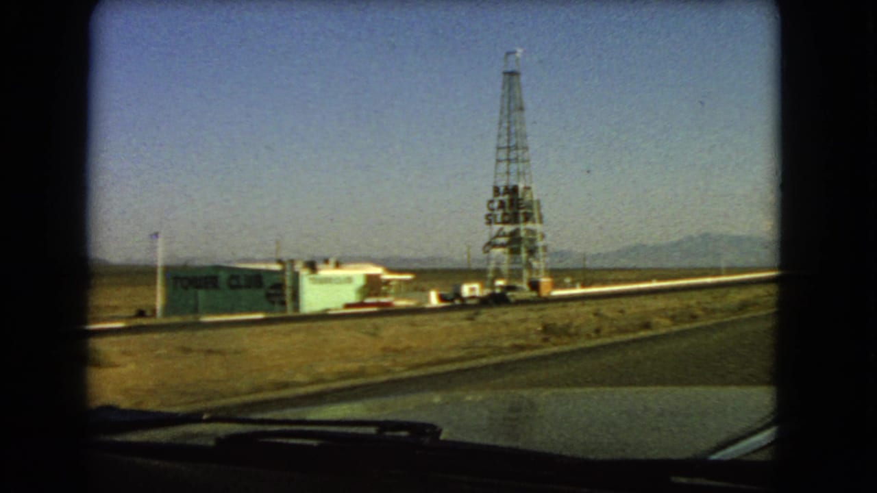 1966 Nevada roadside view from a moving vehicle, showing the Tower Club building and a tall lattice tower sign against distant mountains.