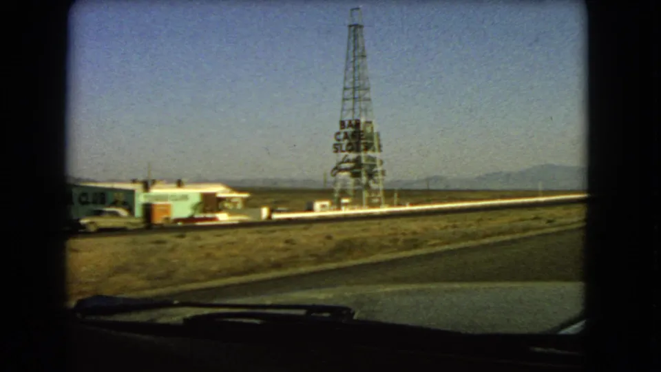 Passenger-window view near Las Vegas in 1966 with a low roadside club, parked car, and tall tower sign beside open desert.