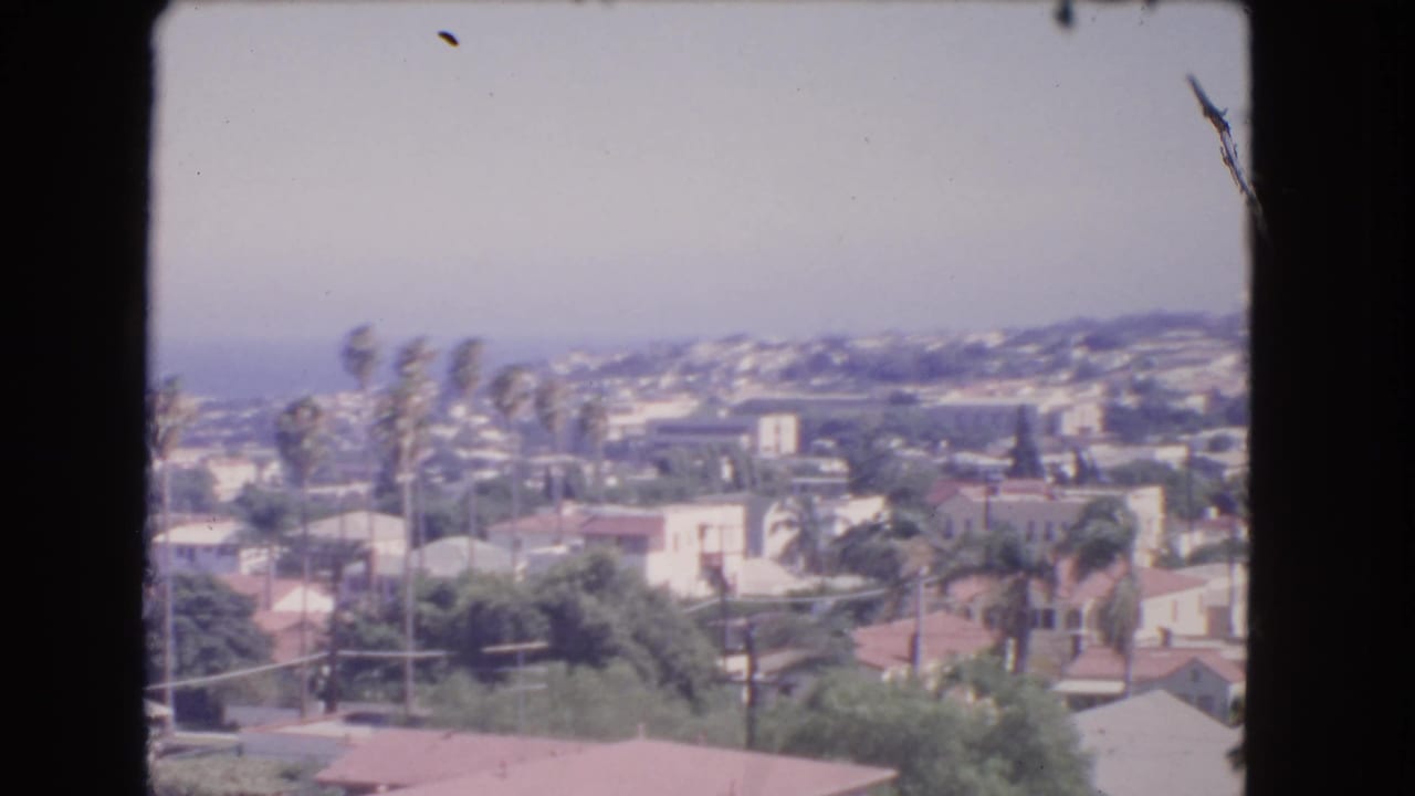1966 8mm view from the Los Angeles heights showing rooftops, palms, greenery, and the Pacific Ocean in haze.