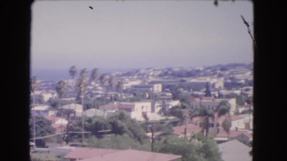 1966 8mm view from the Los Angeles heights showing rooftops, palms, greenery, and the Pacific Ocean in haze.