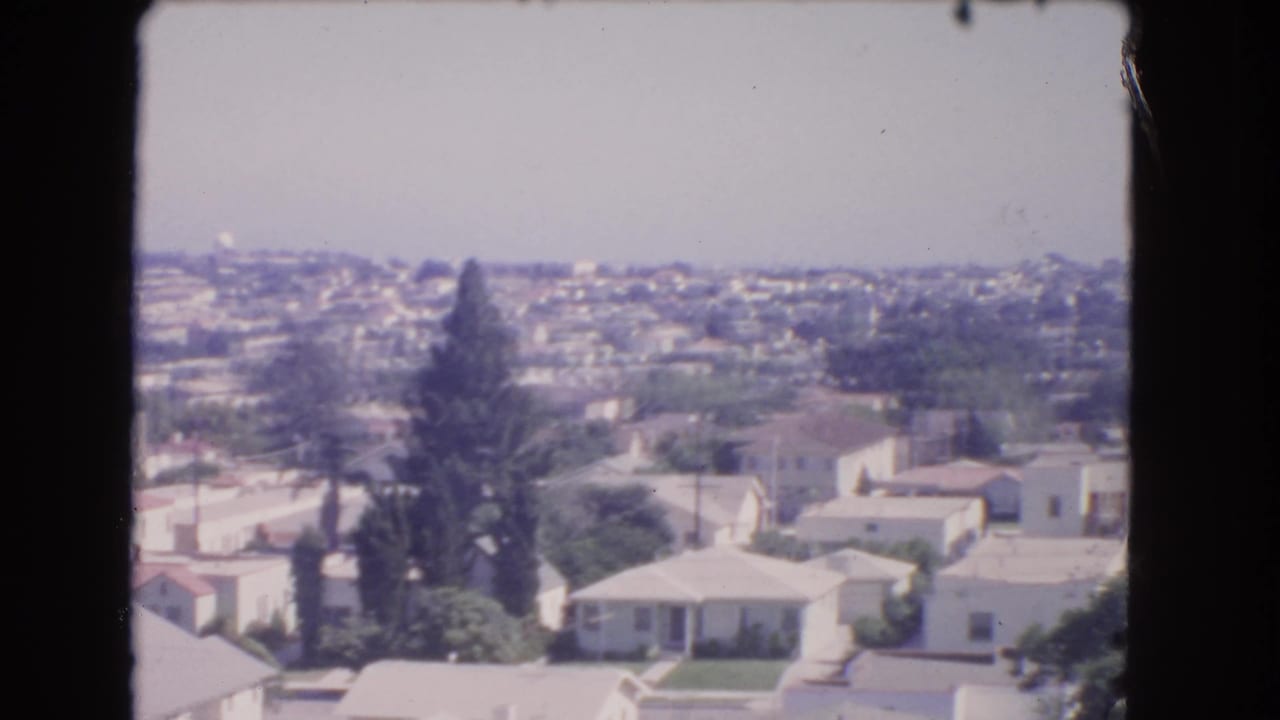 1966 Los Angeles home-movie frame showing hillside suburban homes, trees, and a hazy horizon from an elevated viewpoint.
