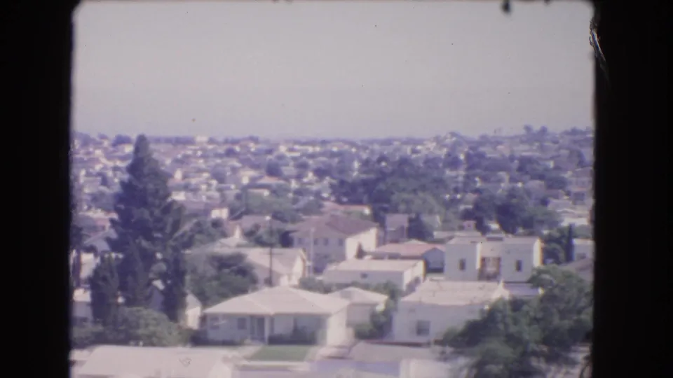 Elevated 1966 Los Angeles view of pale-roofed suburban homes and trees under a hazy sky.