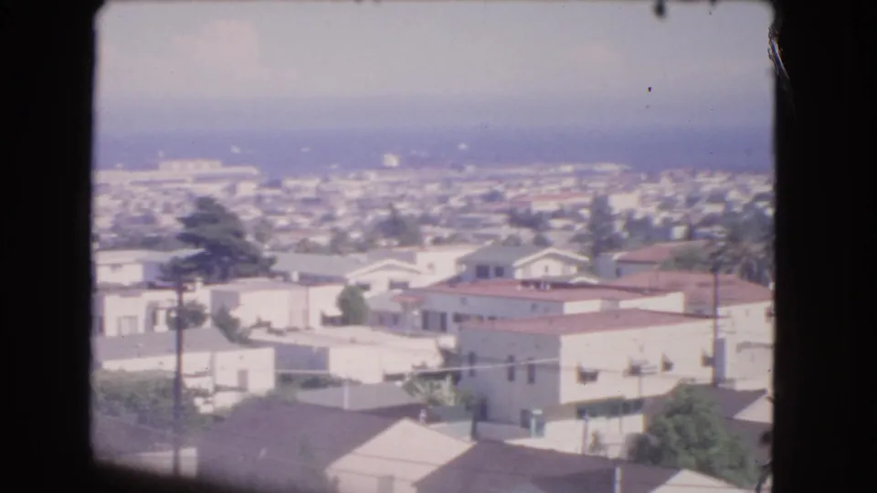 1966 Los Angeles coastal neighborhood view with homes, utility poles, trees, and the Pacific Ocean in haze.