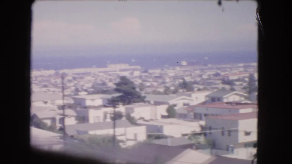 End of a 1966 Los Angeles pan showing suburban homes and utility poles below a hazy Pacific Ocean horizon.