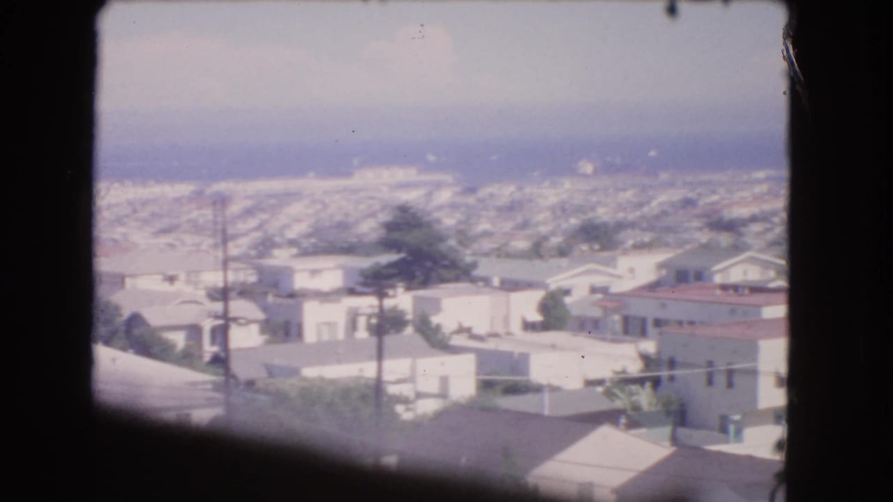 Aerial view of low-rise houses and rooftops seen through a dark airplane window frame.