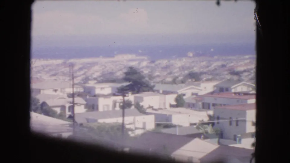 1966 Los Angeles aerial view with suburban rooftops, utility poles, trees, and haze seen through an aircraft window.