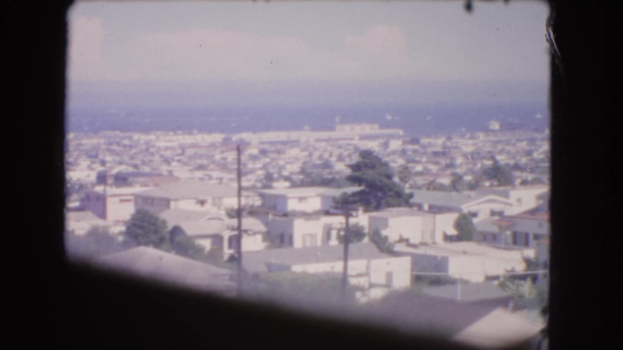 Los Angeles residential blocks and distant haze appear beyond the dark aircraft-window silhouette in this 1966 8mm frame.