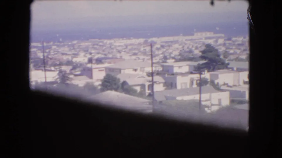 A 1966 Los Angeles airplane-window view shows dense low-rise housing, rooftops, trees, and a hazy skyline area.