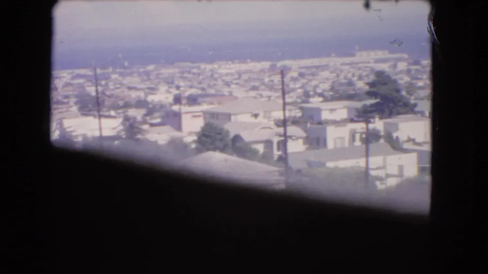 The final 1966 Los Angeles frame keeps the aircraft-window edge in view while showing rooftops, trees, poles, and haze below.