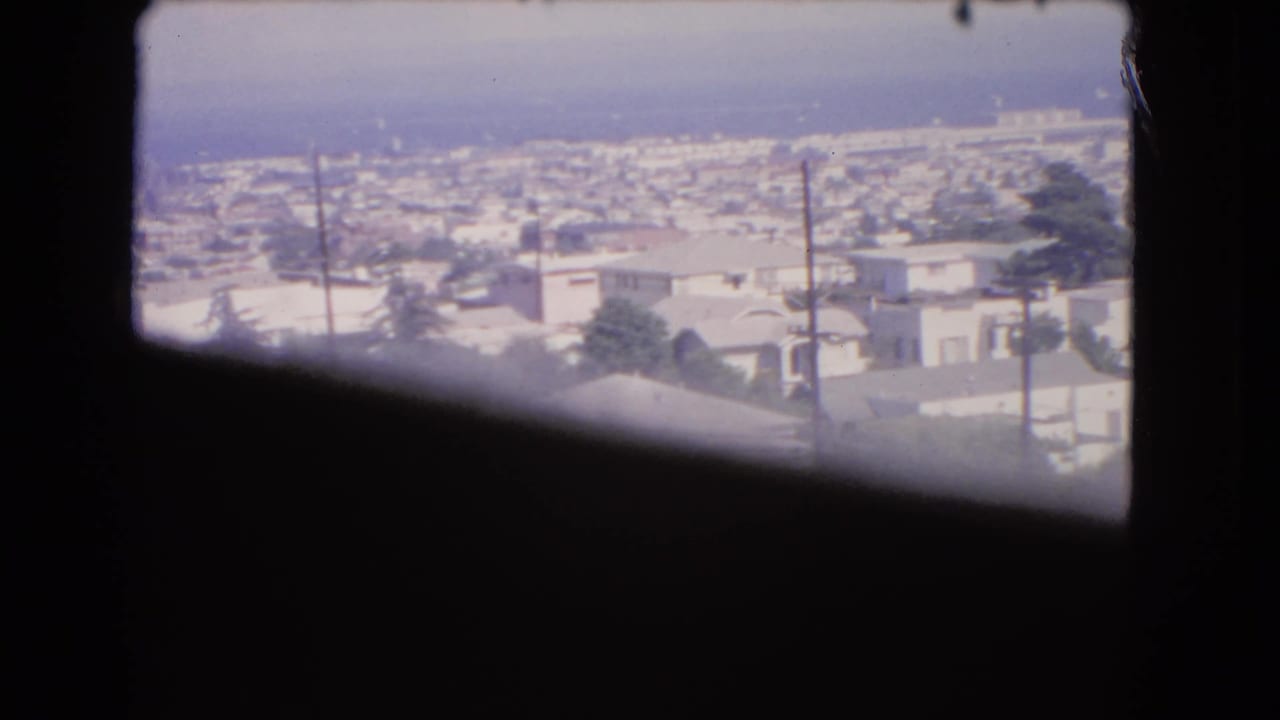 1966 Los Angeles rooftop view through a window, with utility poles in front of low-rise buildings and a hazy ocean horizon.