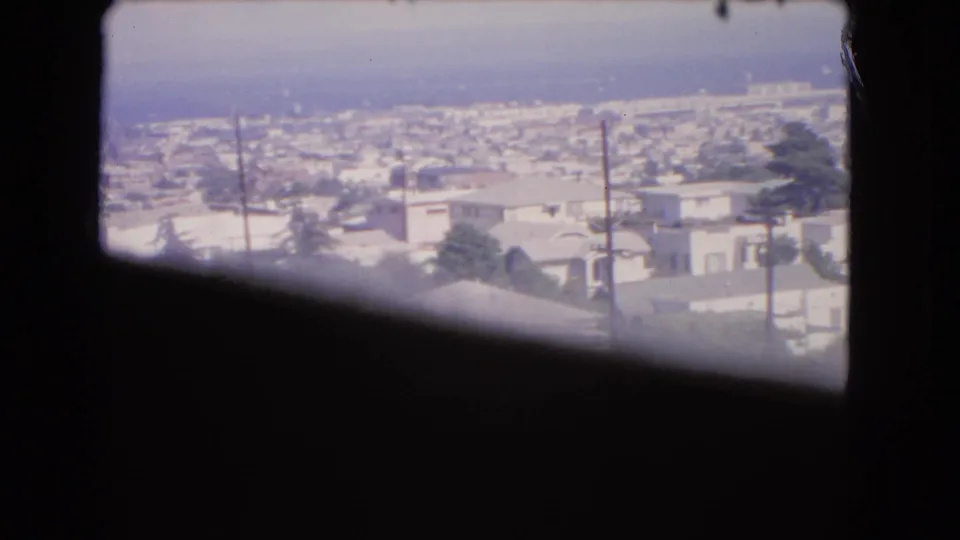 1966 Los Angeles rooftop view through a window, with utility poles in front of low-rise buildings and a hazy ocean horizon.