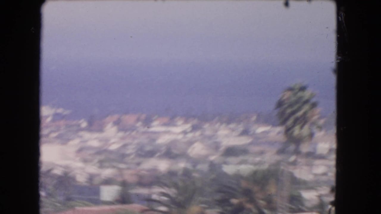 1966 Los Angeles home-movie frame showing a hazy residential panorama with rooftops, trees, palms, and a distant blue horizon.