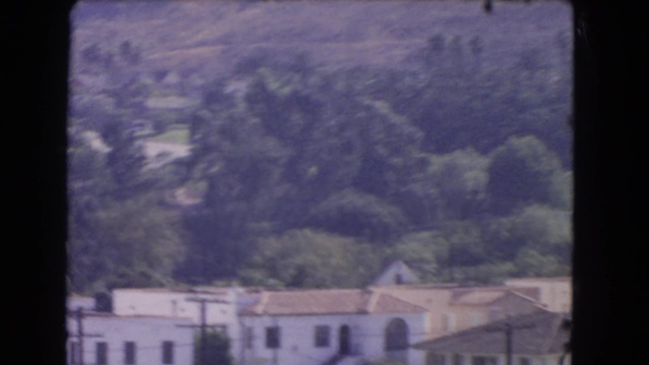 Elevated 1966 Los Angeles neighborhood view with distant hillside trees and pale homes partly softened by 8mm focus.