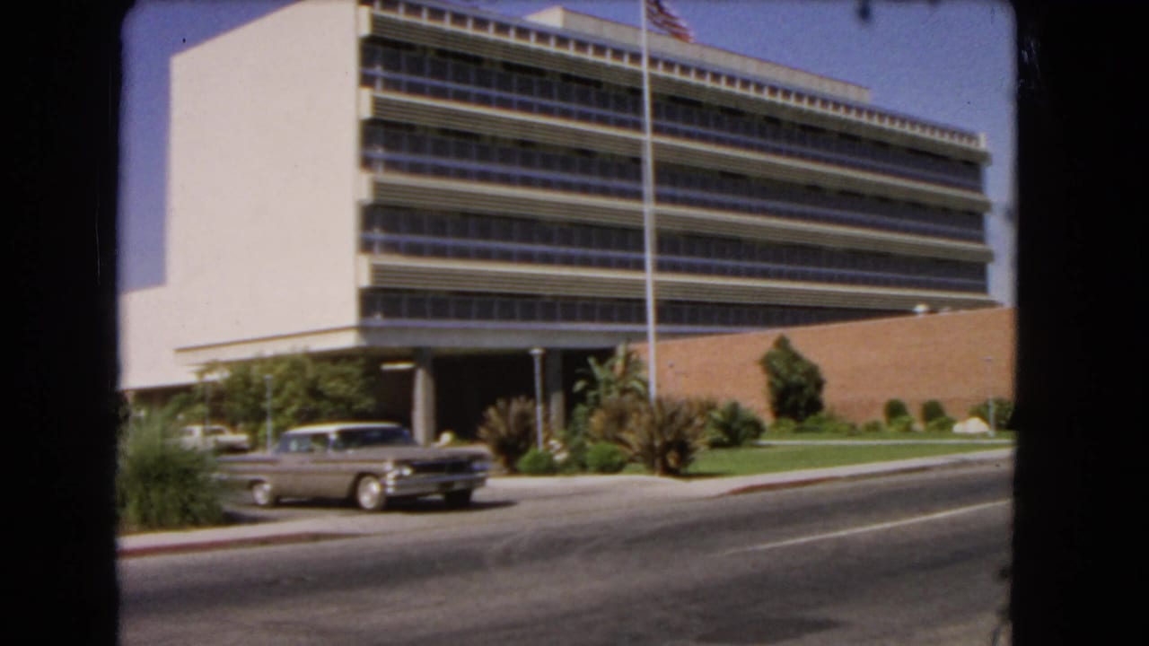Classic sedan moving along the street in front of a large office building.