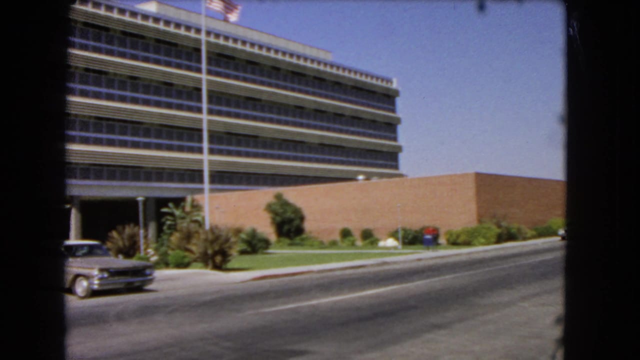 Large office building beside a road with a light-colored sedan entering from the left.