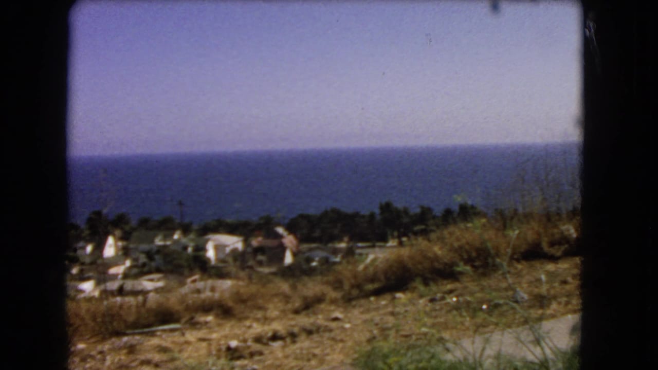 1966 Los Angeles-area 8mm frame showing a dry hillside foreground, scattered coastal homes, trees, and the Pacific horizon.