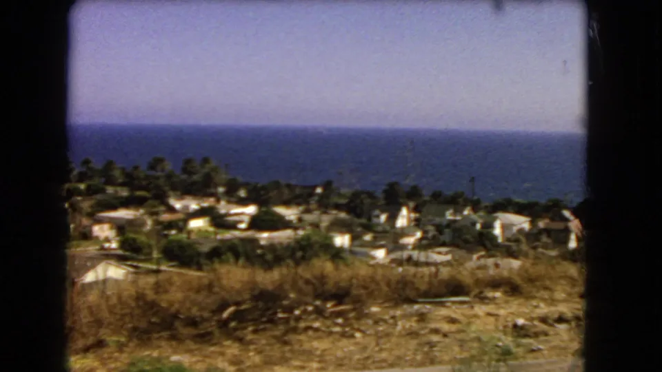 Los Angeles coastal homes, palms, dry foreground brush, and a clear ocean horizon appear in this 1966 8mm frame.
