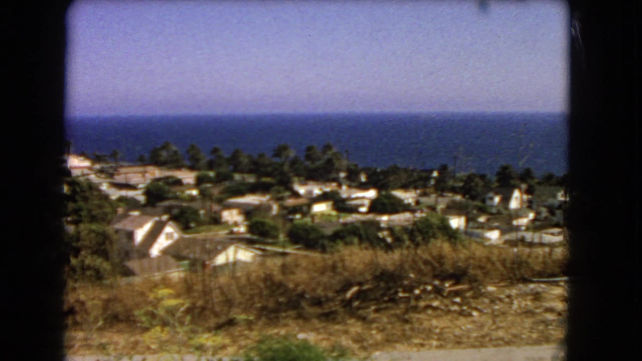 1966 Los Angeles-area 8mm frame showing dry hillside grass, houses, trees, and the Pacific Ocean horizon.