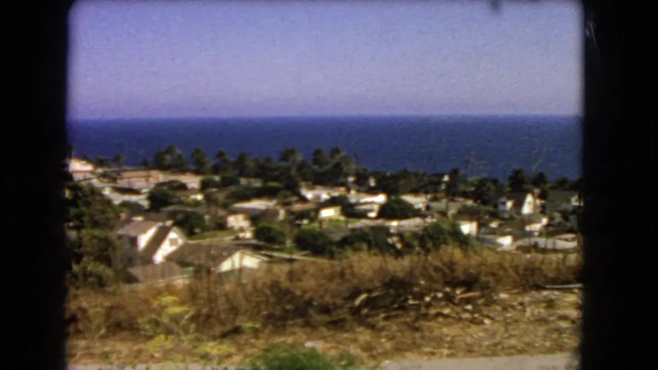 1966 Los Angeles-area 8mm frame showing dry hillside grass, houses, trees, and the Pacific Ocean horizon.