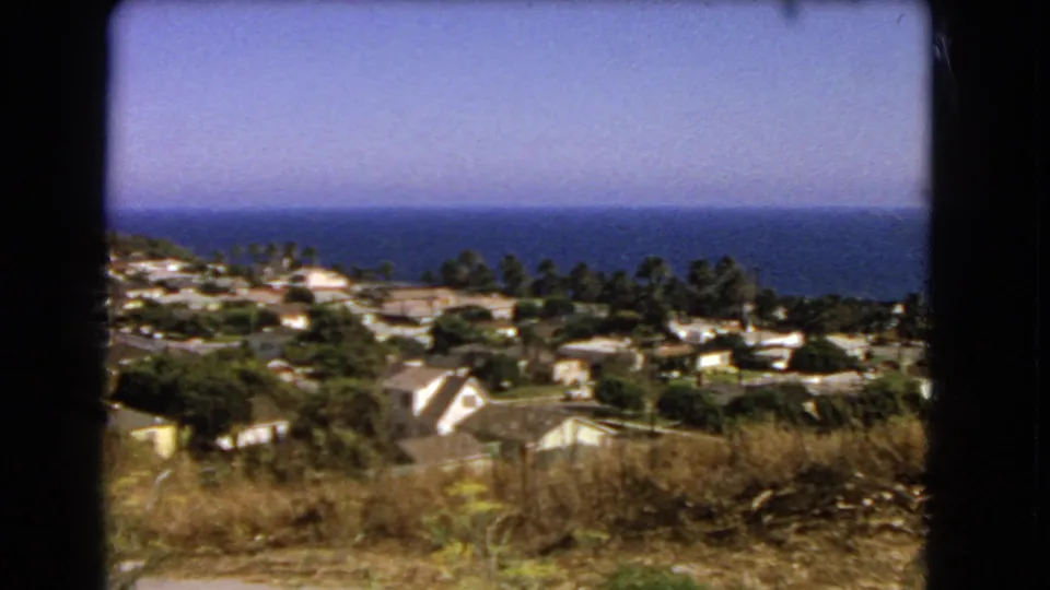 1966 Los Angeles-area 8mm view across hillside brush and rooftops toward the Pacific Ocean under a clear sky.