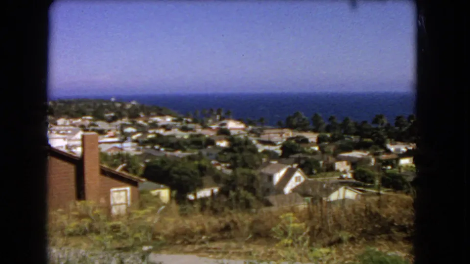 1966 Los Angeles coastal neighborhood seen from above, with a brick chimney, rooftops, trees, dry grass, and the Pacific Ocean beyond.