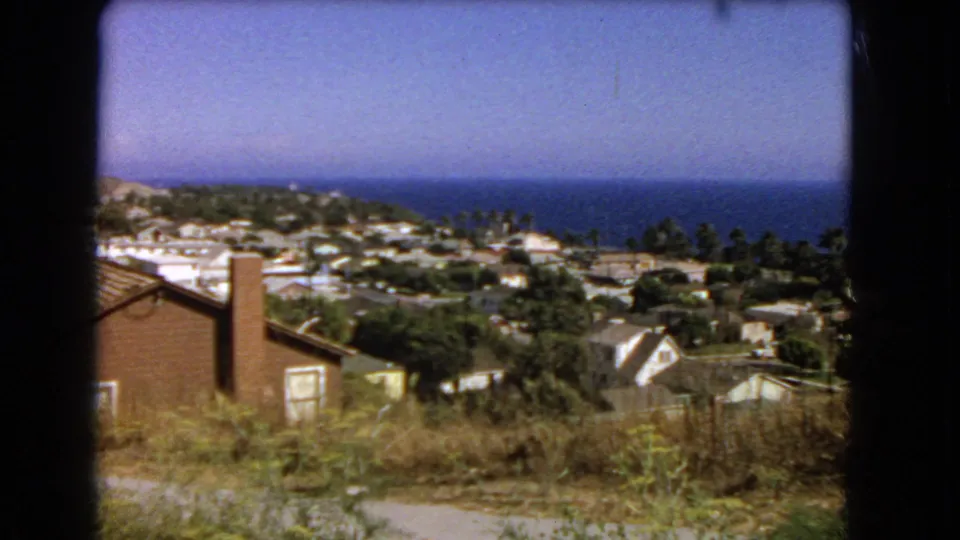 Elevated 1966 Los Angeles view showing a brick house edge, residential rooftops, palms or trees, and the Pacific Ocean in the distance.