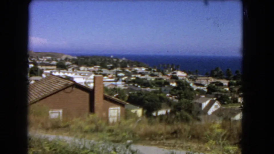 End frame of the 1966 Los Angeles coastal view, with a brick chimney, dry hillside vegetation, clustered houses, trees, and Pacific horizon.