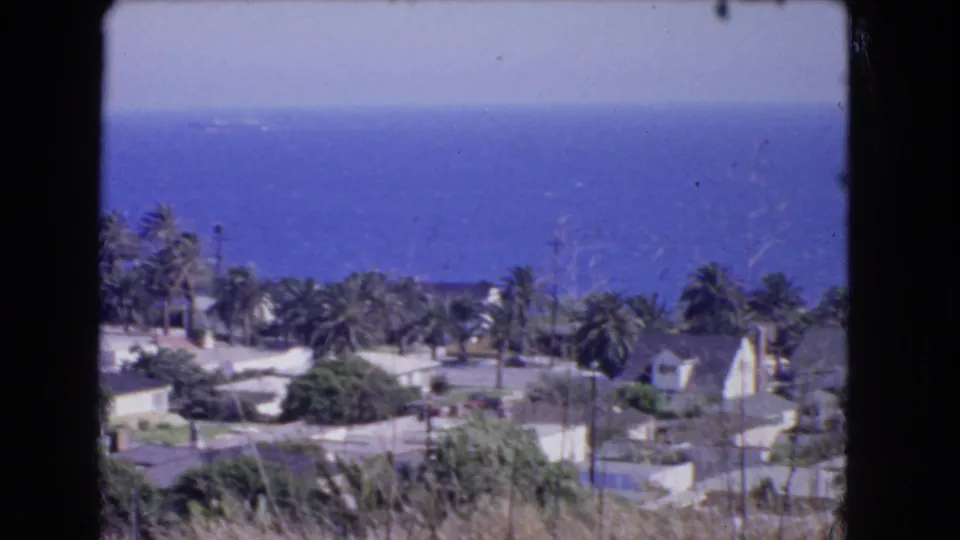Coastal Los Angeles view looking past palm trees and rooftops toward a broad blue ocean in a 1966 8mm home movie frame.