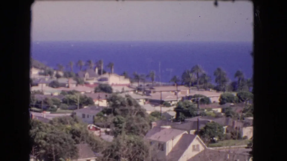The frame looks across a Los Angeles coastal residential area in 1966, with roads, trees, roofs, palms, and the Pacific horizon.