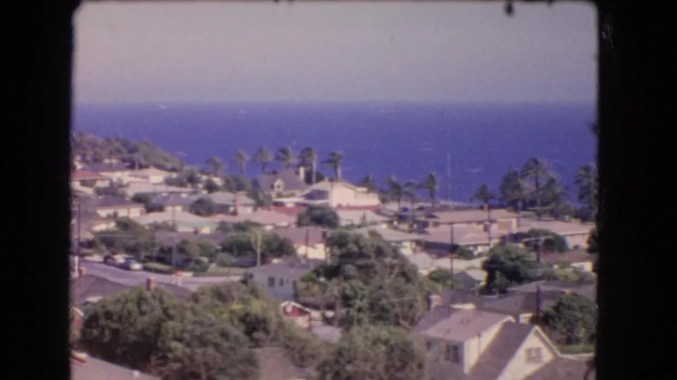 A high view over 1966 Los Angeles coastal homes shows palms, rooftops, vegetation, and a deep blue Pacific horizon.