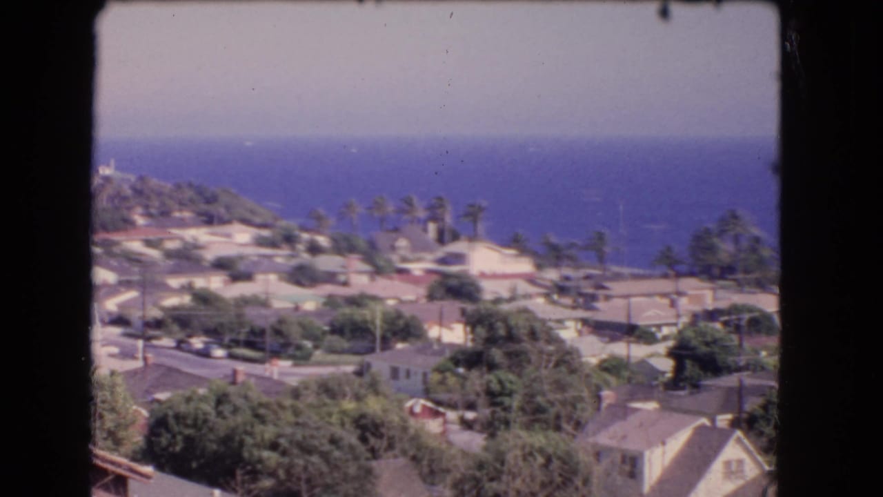 1966 Los Angeles coastal neighborhood seen from above, with rooftops, palms, trees, and the Pacific Ocean in the distance.