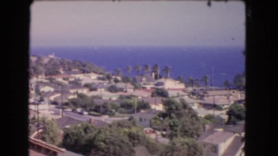Los Angeles coastal hillside neighborhood in 1966, showing clustered homes, palm trees, and ocean beyond the rooftops.