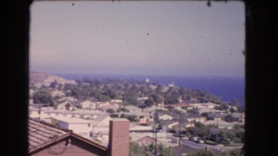 Elevated 1966 Los Angeles coastal view with tiled roof, chimney, hillside homes, palms, and blue ocean beyond.