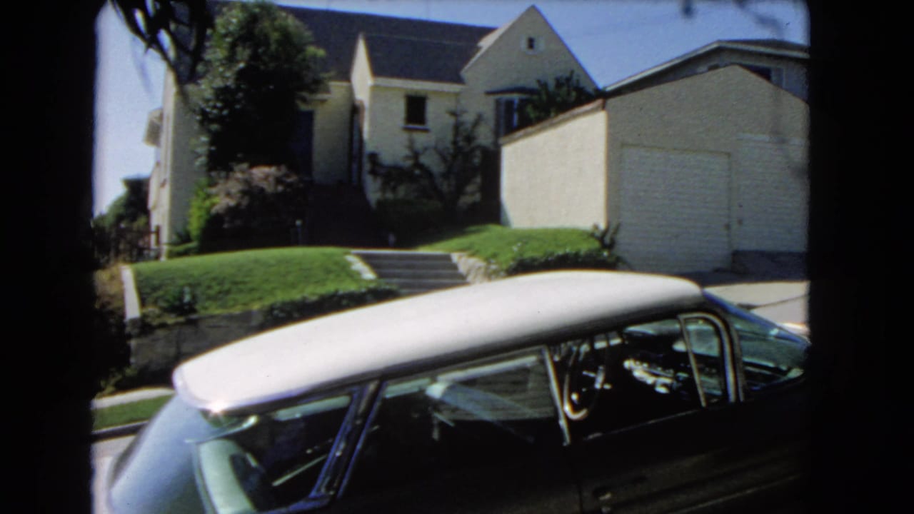 Suburban house with lawn steps and a parked classic car in bright sunlight.