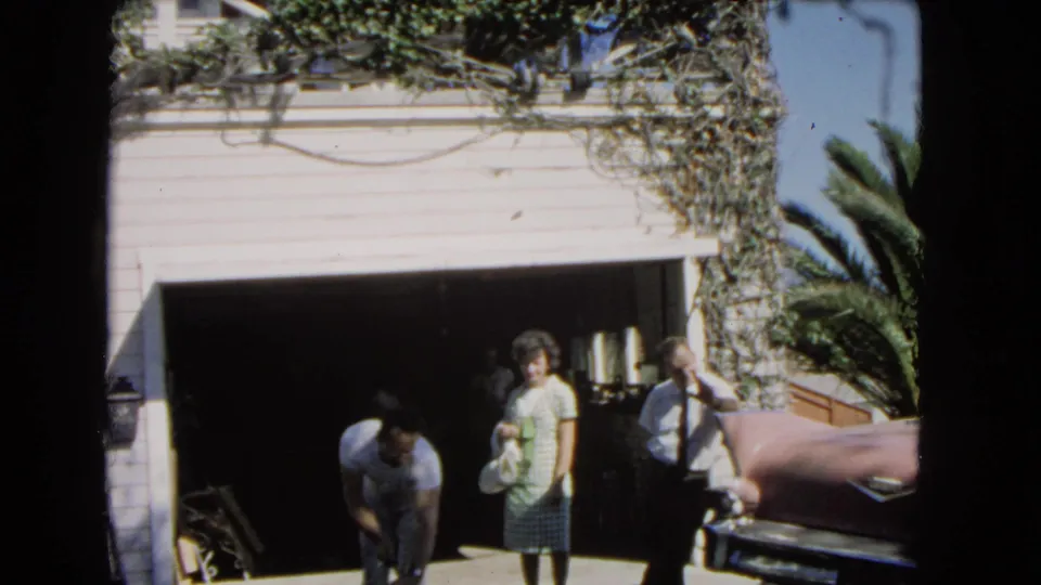 1966 Los Angeles suburban driveway view with an open garage, standing couple, and Black man working in the foreground.