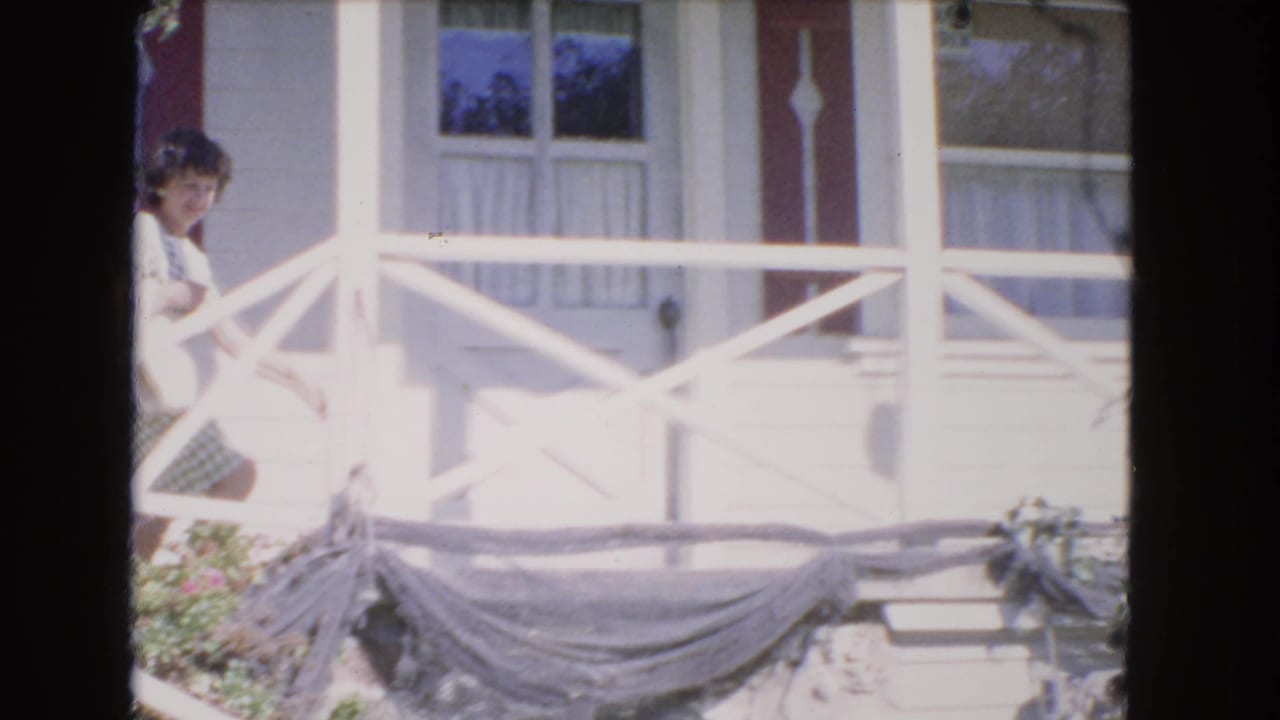 Young woman standing near a white front porch railing outside a house.
