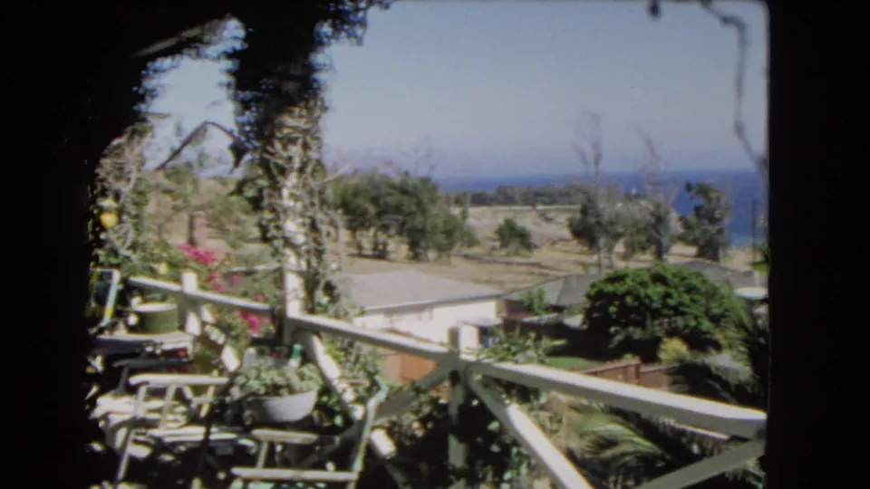 1966 Los Angeles 8mm frame showing a balcony garden and seating area looking across hillside trees toward the distant ocean.