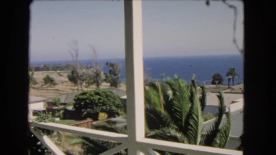 Soft 8mm frame of a Los Angeles-area balcony view, with palms and low coastal homes leading toward the Pacific horizon.