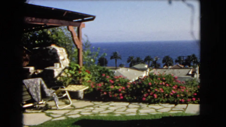 1966 Los Angeles 8mm frame showing a pergola-side garden patio looking out over palms, rooftops, and the ocean.
