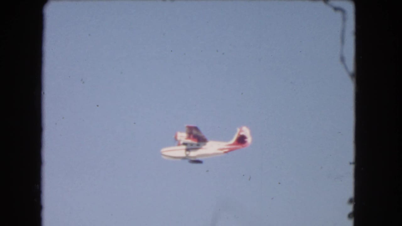 Small red-and-white seaplane crosses a clear blue sky.
